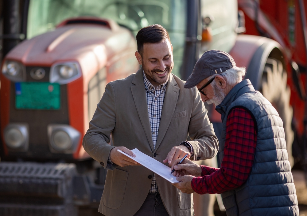 Senior,farmer,signing,contract,with,businessman,in,front,of,tractor